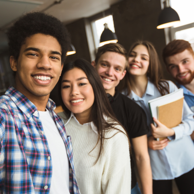 A diverse group of five young adults smiling and posing for a selfie in a modern interior setting.